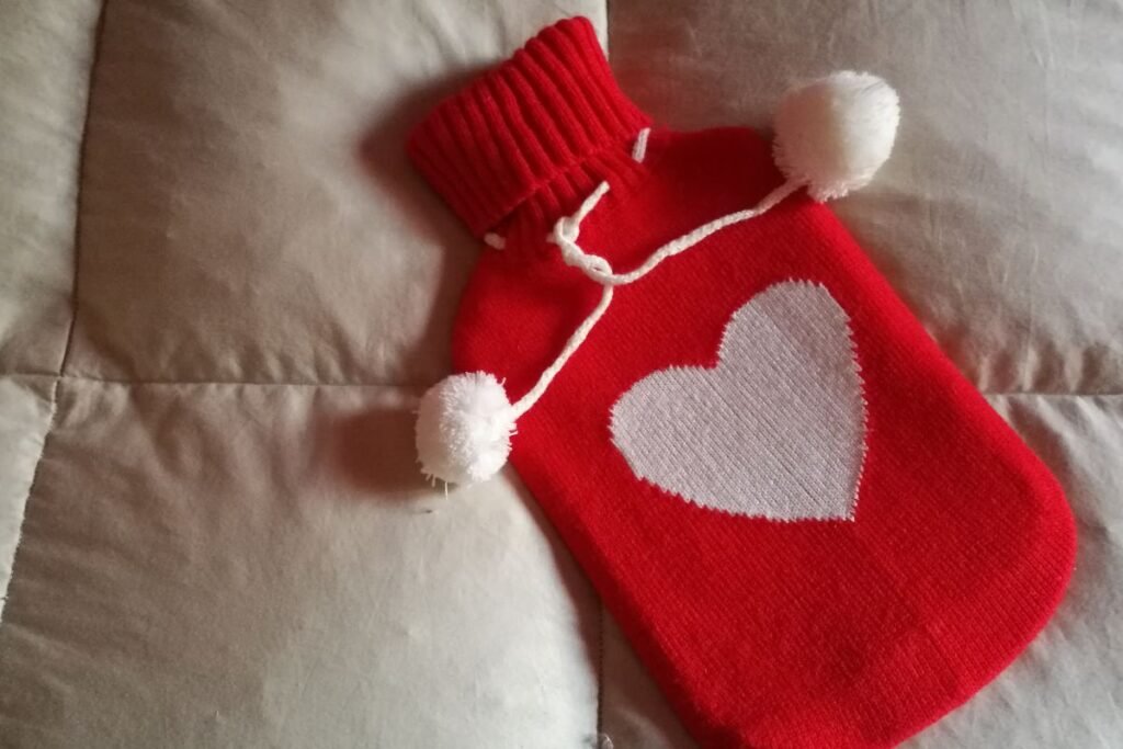 Bouillotte tricotée rouge avec des pompons, sur une couette douillette un cocon chaleureux pour affronter le froid.