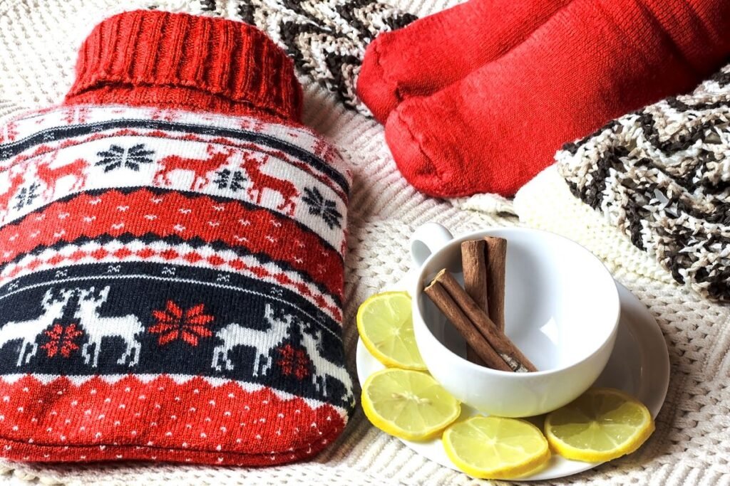 Instant cocooning avec bouillotte, chaussettes rouges et infusion citron-cannelle sur plaid douillet.