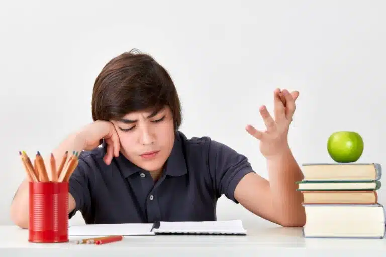 Adolescent exaspéré à son bureau devant un cahier, des crayons et des livres, illustrant les difficultés d'attention et d'organisation liées au TDAH