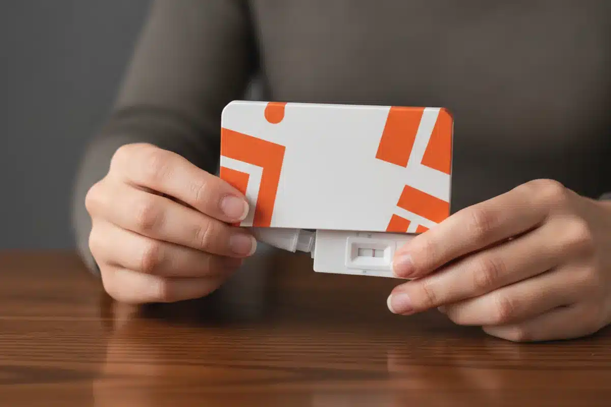 Test rapide de la grippe en boîte blanche et orange mains tenant un kit de test rapide grippe sur table en bois