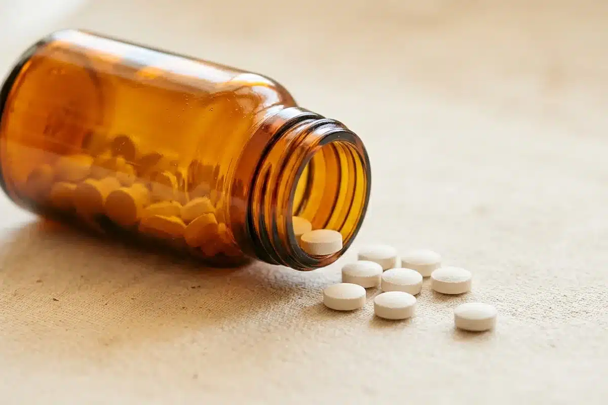 Comprimes de cortisone voie orale Flacon de medicaments avec des comprimes de cortisone sur une surface beige, representant la voie orale d administration
