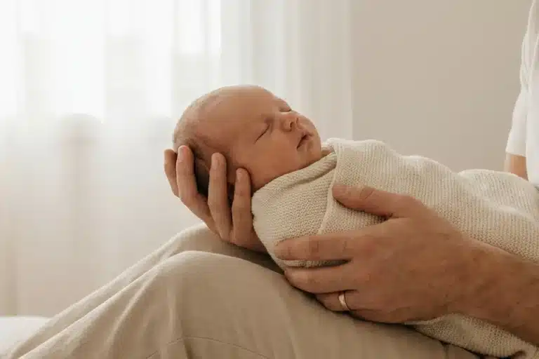 Mains adultes soutenant délicatement la tête et le dos d'un nourrisson nouveau-né, geste doux et sécurisant