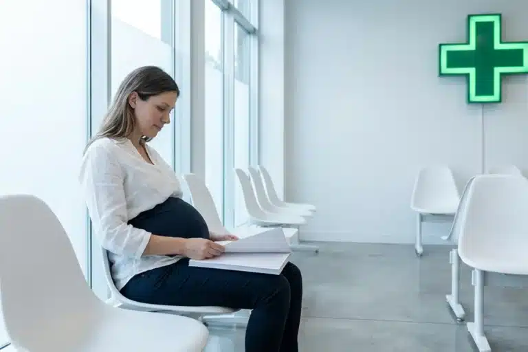 Femme enceinte en salle d'attente médicale regardant des documents administratifs