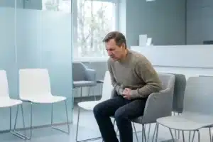Patient dans une salle d'attente médicale tenant son ventre, illustrant la question : peut-on mourir d'un ulcère à l'estomac ?