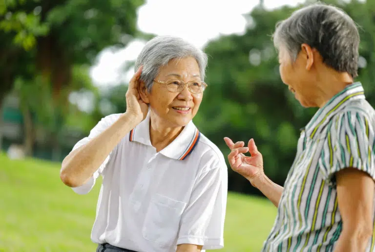 Femme senior portant la main derrière son oreille pour mieux entendre une amie lors d'une conversation en extérieur