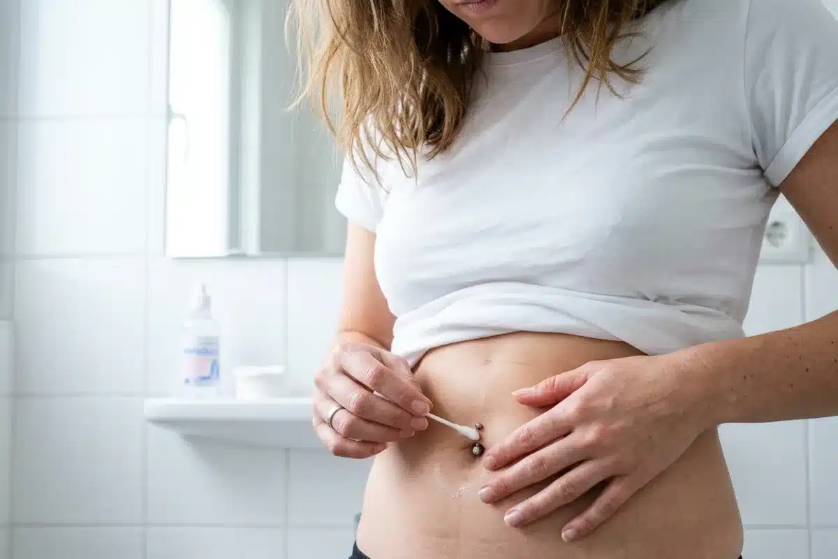 Soins antiseptiques pour un piercing au nombril Personne appliquant un coton avec sérum physiologique sur un piercing au nombril : soin quotidien pour éviter le rejet