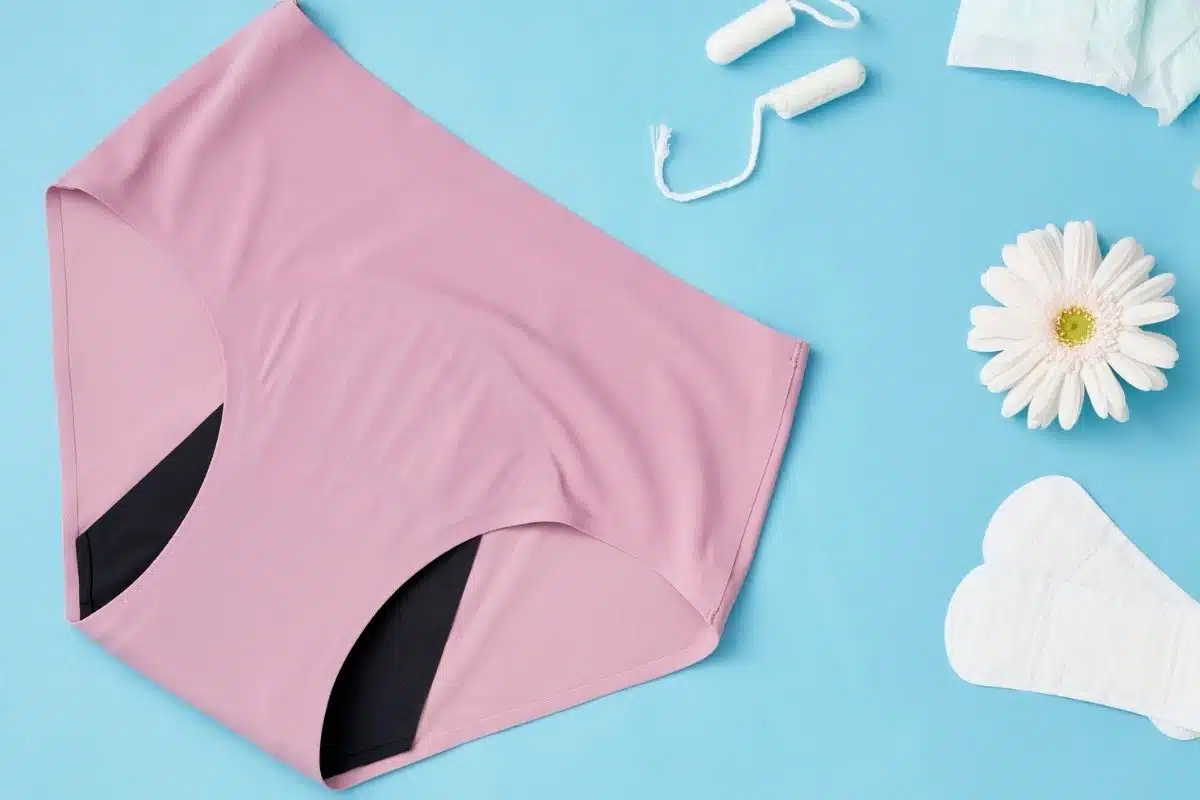 Culotte menstruelle et autres protections hygiéniques Culotte menstruelle rose à zone absorbante, posée avec un tampon et des serviettes sur fond bleu