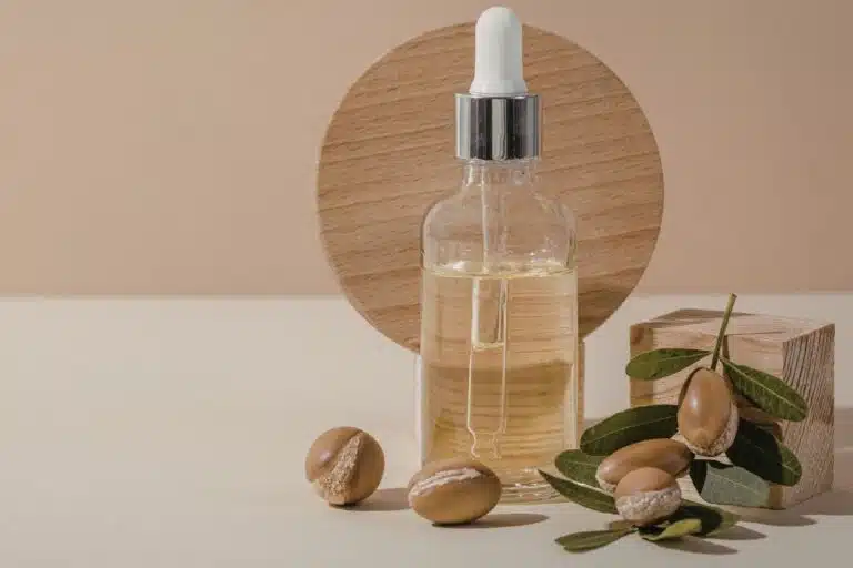 Flacon d'huile d'argan bio avec pipette, amandons d'arganier et feuilles sur fond beige