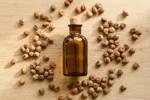 flacon d'huile de souchet posé sur fond de bois naturel entouré de noix tigrées séchées