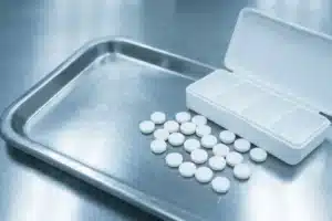 Comprimés blancs ronds de lithium éparpillés depuis un pilulier sur un plateau médical inox, thymorégulateur de référence pour le trouble bipolaire