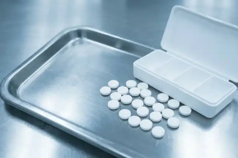 Comprimés blancs ronds de lithium éparpillés depuis un pilulier sur un plateau médical inox, thymorégulateur de référence pour le trouble bipolaire