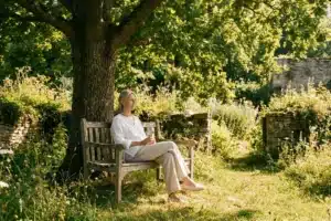 Femme âgée assise à l'ombre dans un jardin, tenant une bouteille d'eau par forte chaleur (stent et chaleur)